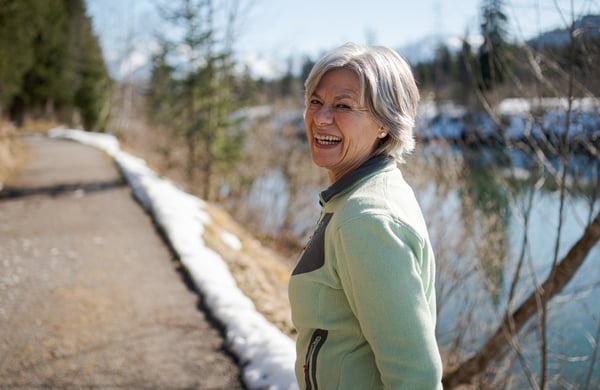 Kvinna med grått hår promenerar på en stig bredvid en sjö