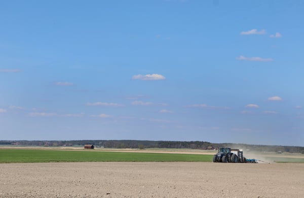 Vy över vårbruk - blå himmel och därunder en åker med traktor