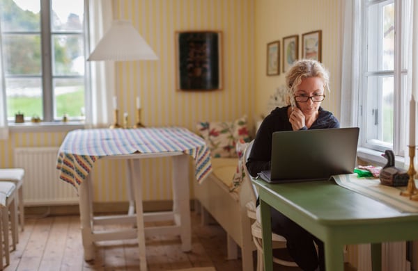 Kvinna sitter vid dator och håller en telefon i handen