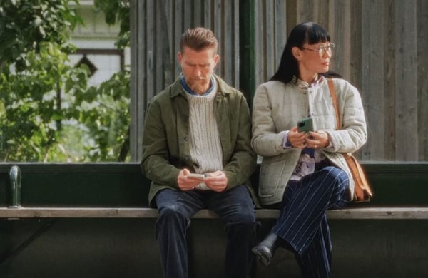 Två personer på en bänk med mobiltelefoner i händerna