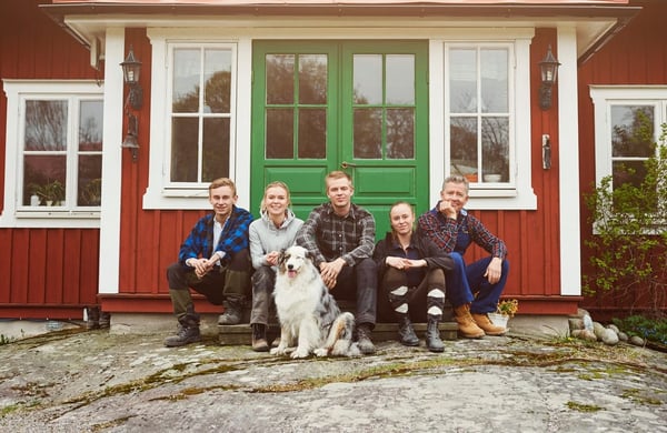 Familj sitter utanför entrén  till ett rött hus med gröna dubbeldörrar.