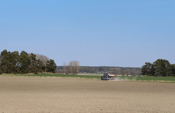 Vy över åker och blå himmel, traktor och såmaskin på avstånd