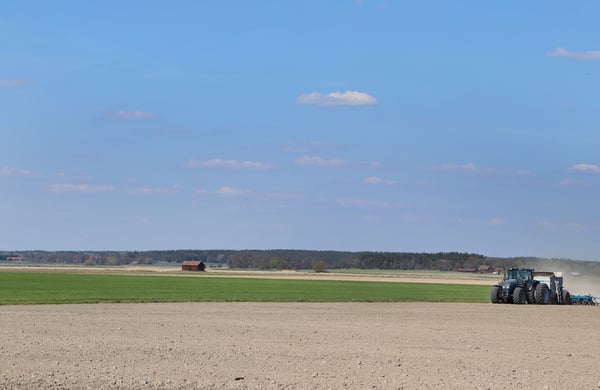 Vy över åker och blå himmel, traktor och såmaskin på avstånd