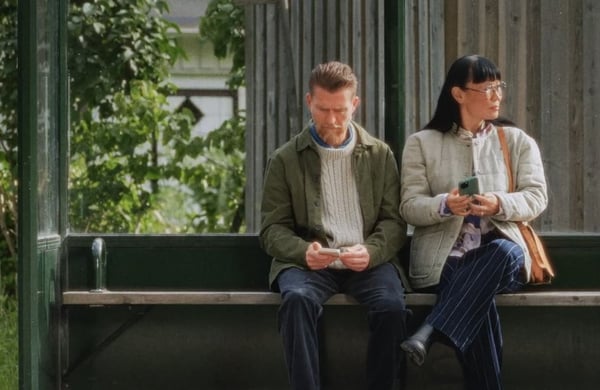 En man och en kvinna sitter i en busskur med sina telefoner i handen