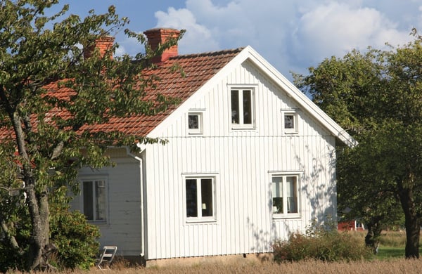 Vitt hus på landsbygden omringat av sädesfält och fruktträd.