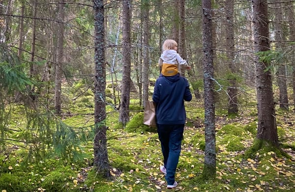 Man promenerar i skogen med barn på axlarna