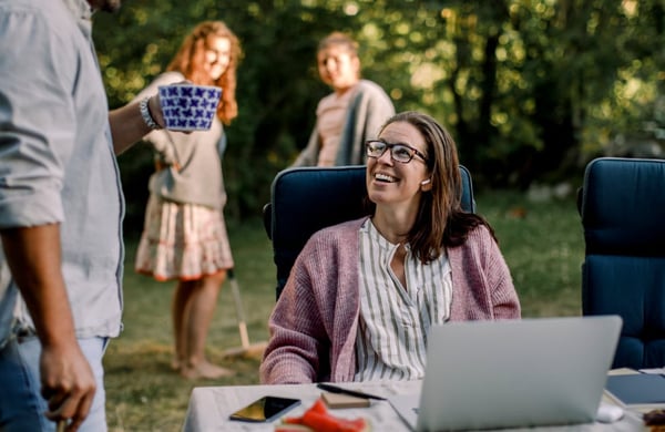 Leende kvinna sitter vid dator och tittar upp mot en man.