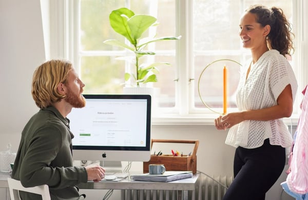 Man sitter framför datorn. Kvinna står bredvid.