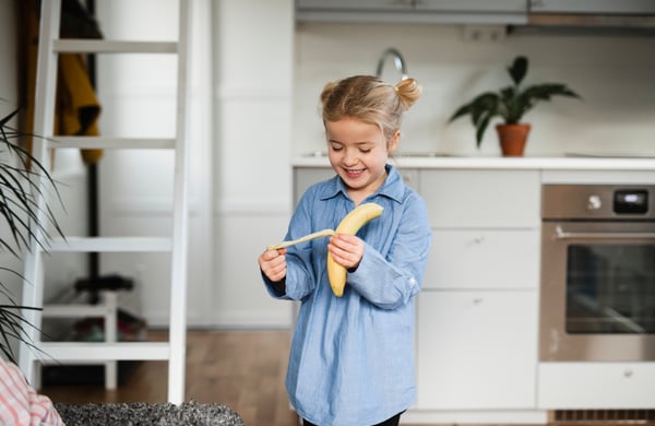 Flicka står i ett kök och äter en banan