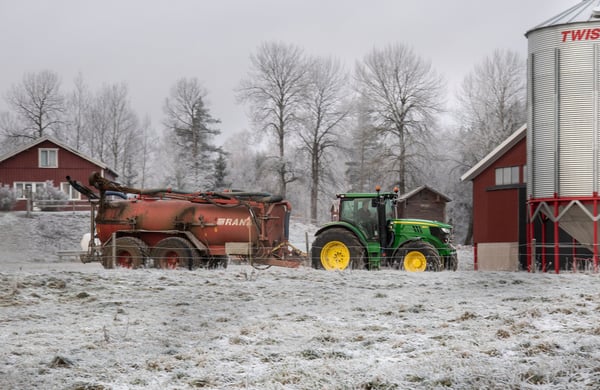 En snöklädd bondgård med en traktor som drar ett släp