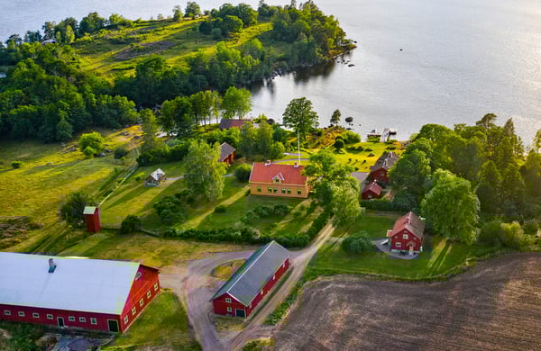 Flygfotografi över sjönära gård i vackert solljus.