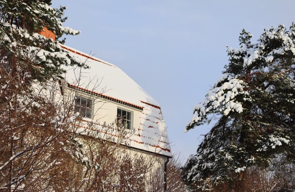 Vitt hus med snö på taket. Snöbeklädda träd i framkant.