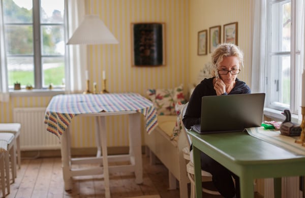 Kvinna sitter vid dator och håller en telefon i handen