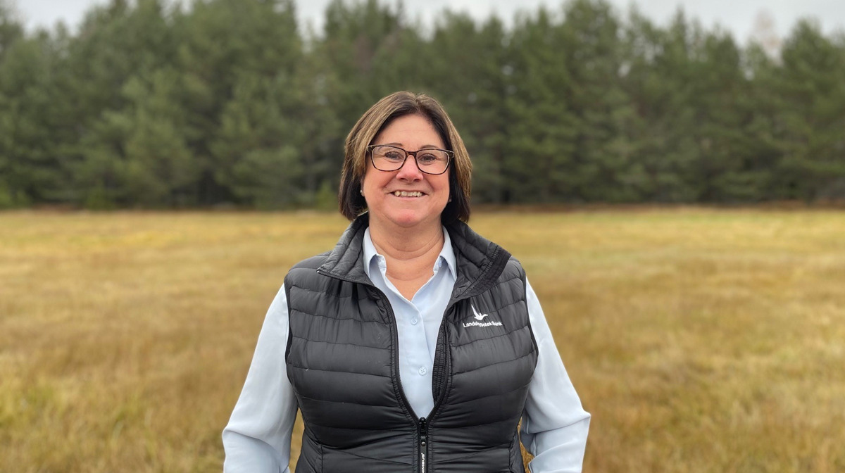 Katarina Johansson st&aring;r framf&ouml;r ett f&auml;lt med skog i bakgrunden.